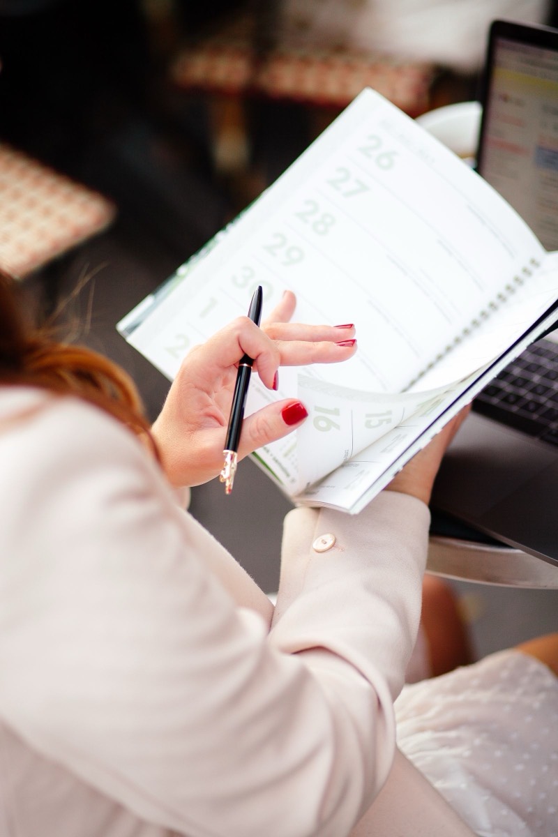 Close-up of hands writing in a planner, laptop in the background