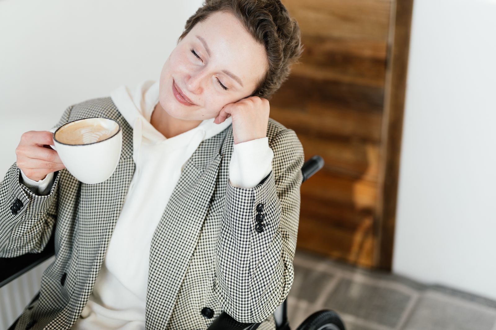A woman using a wheelchair, eyes closed, enjoying a coffee.